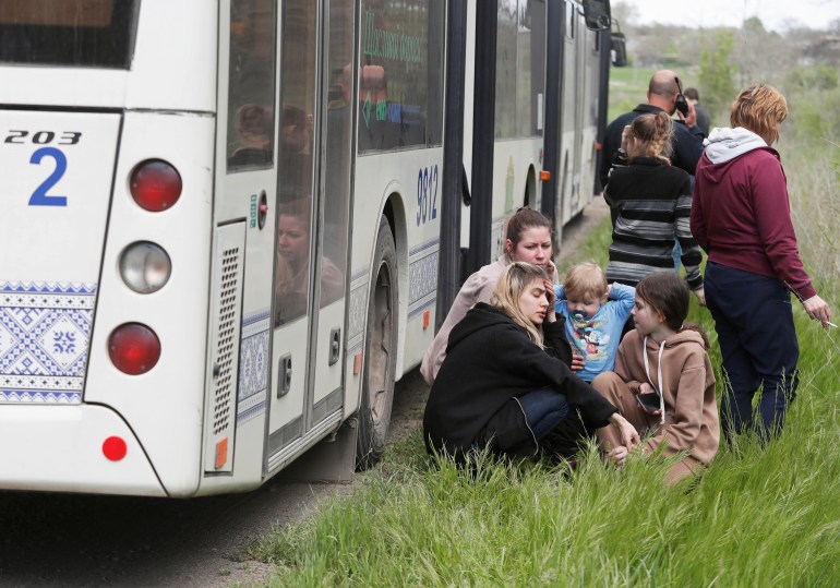 People rest next to a bus as civilians from Mariupol, including evacuees from Azovstal steel plant, travel in a convoy to Zaporizhzhia