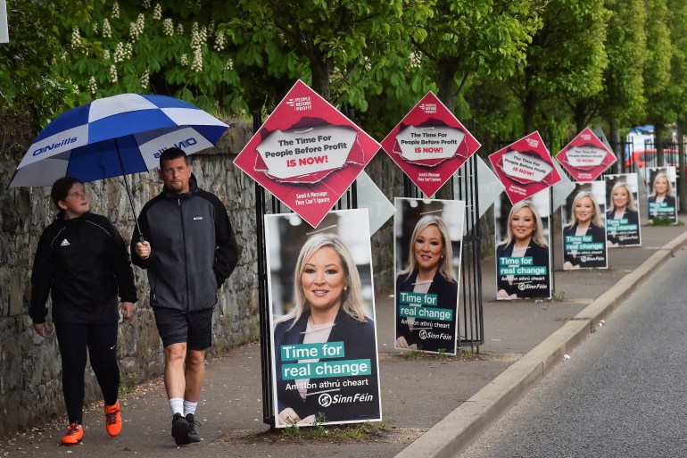 People walk past Election posters of Sinn Fein party Vice President Michelle O'Neill along the nationalist Falls Road, in Belfast