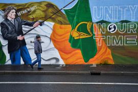 A man walks past a mural along the nationalist Falls Road, in Belfast