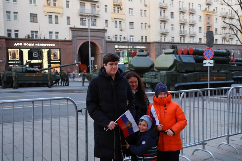 People pose as military vehicles drive along a street during a rehearsal for the Victory Day military parade in Moscow
