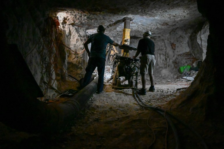 A photo of two people standing in a mine with mining equipment.