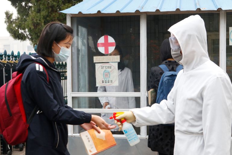 A schoolgirl in a face mask has her hands disinfected by a worker in a hazmat suit at the entrance to a Pyongyang secondary school
