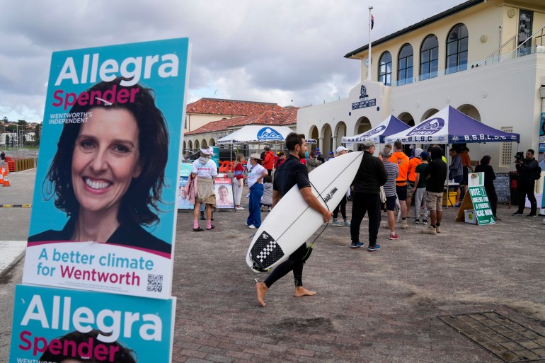 A man in a wetsuit and surf board joins the queue to vote at a Bondi Beach polling station