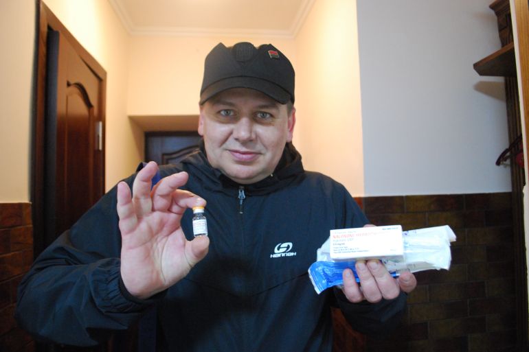A photo of a man holding a box of medication with his left hand and a little vile of liquid with his right.