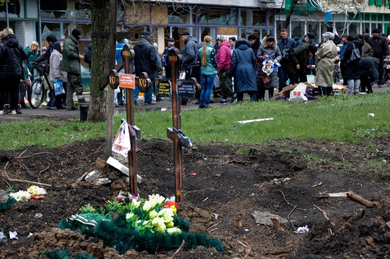 Local residents gather at a makeshift street market next two fresh graves in the foreground in an area controlled by Russian-backed separatist forces in Mariupol, Ukraine, Friday, April 22, 2022