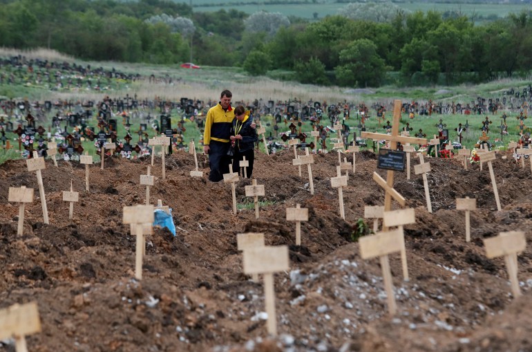 People stand amid newly-made graves at a cemetery in the town of Staryi Krym outside Mariupol, Ukraine May 22, 2022