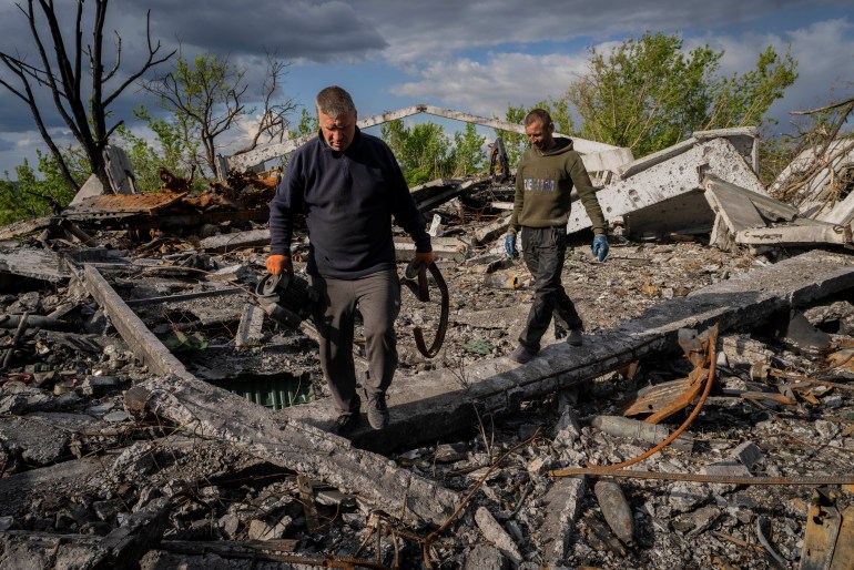 Villagers walk past unexploded artillery shells as they collect scrap metal from a bombed warehouse in the village of Malaya Rohan, Kharkiv region.