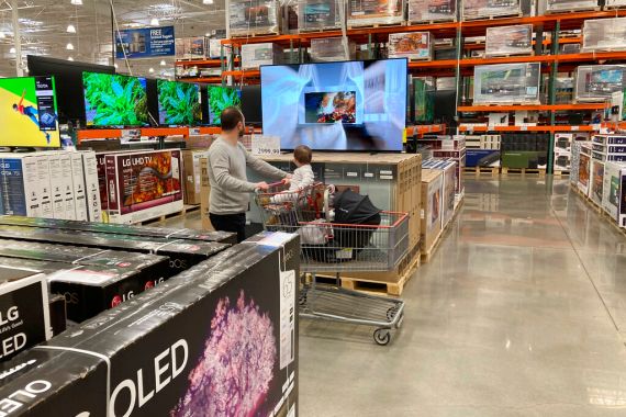 A shopper pushes a child in a cart while browsing at big-screen televisions