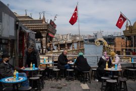 People sit and eat on tables in front of the water and a turkish flag