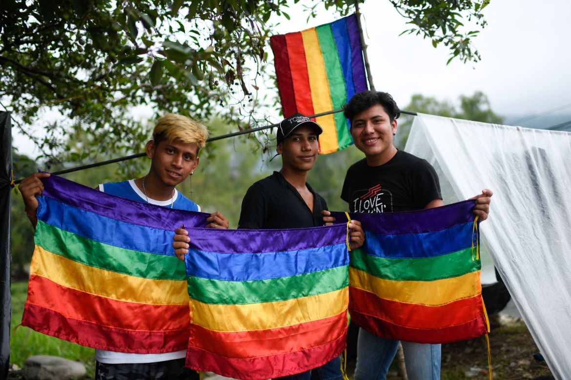 Guatemalan migrants Estuardo Mejia (L), Jeferson Rodriguez (R) and Venezuelan migrant Luis Villalobos, who are part of a caravan heading to the US, pose with rainbow flags at a makeshift camp in Huixtla, Chiapas state