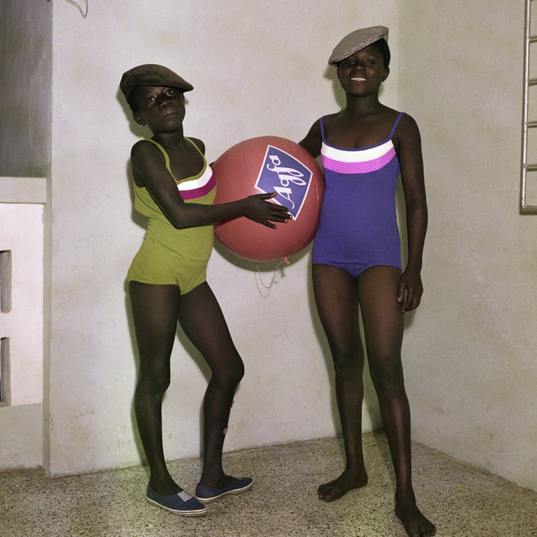 A photo of two people in swimsuits, the one on the left is holding a large ball.