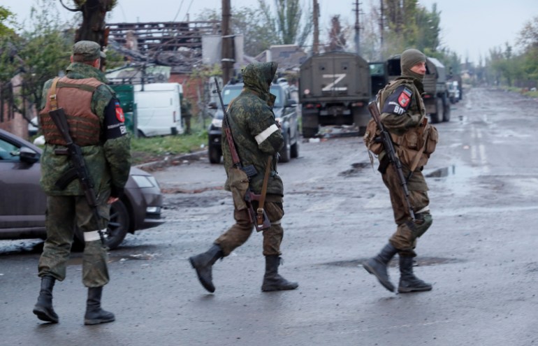 Service members of pro-Russian troops walk across a road before the expected departure of Ukrainian soldiers