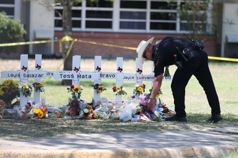 A police officer sets flowers from someone mourning at a memorial at Robb Elementary School