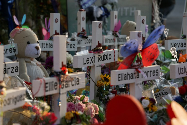 Flowers, toys, and other objects lay by crosses representing the 19 schoolchildren killed in Uvalde, Texas