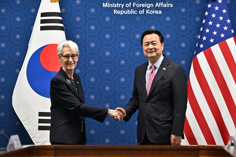 Wendy Sherman, standing in front of a South Korean flag, shakes hands with South Korea's First Vice Foreign Minister Cho Hyun-dong who is in front of a US flag