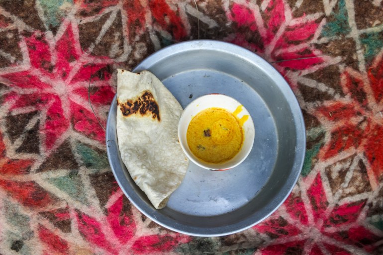 An overhead view of a metal tray with one bowl of golden kudan on it and a roti