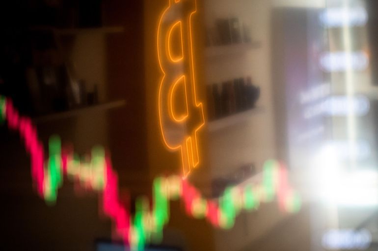 A reflection of a candlestick price chart and an illuminated Bitcoin logo inside a BitBase cryptocurrency exchange in Barcelona, Spain
