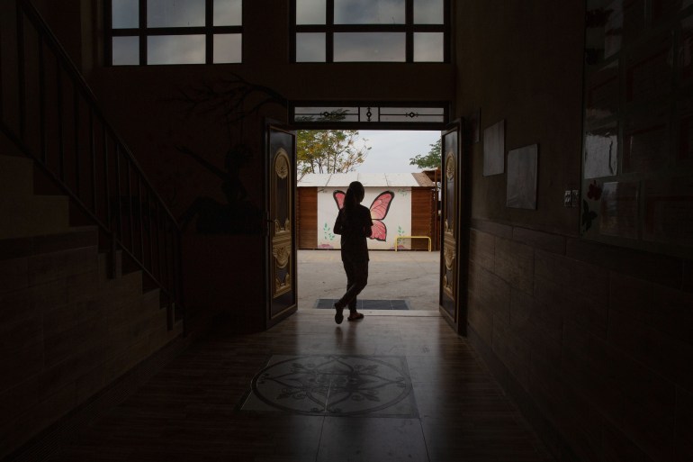 A photo of the silhouette of someone standing in a doorway leading outside.