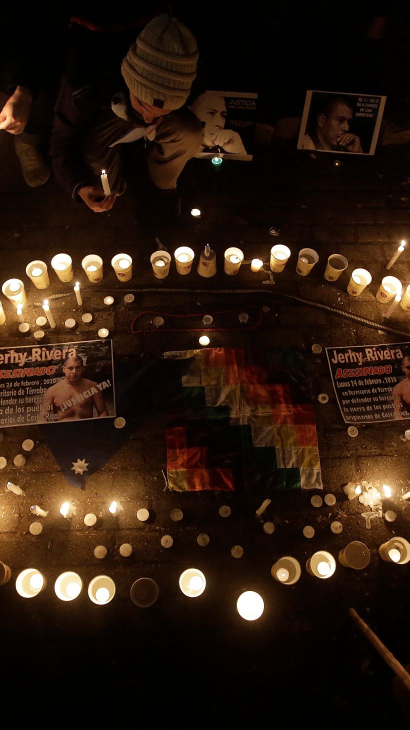 A photo of a vigil held to mourn the death of Jerhy Rivera with a circle of candles with photos of Jerhy Rivera in and around it, with people sitting around the circle..