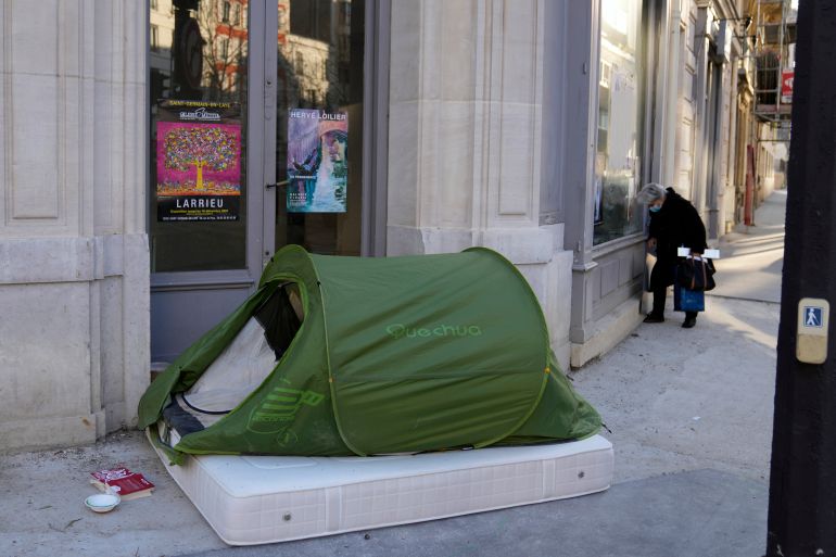 A woman stands in a street next to a homeless tent, in Paris