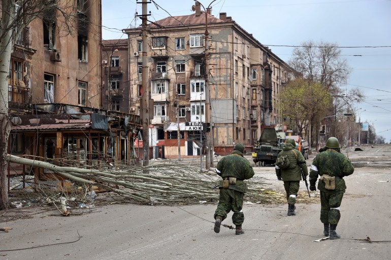 FILE - Servicemen of the militia from the Donetsk People's Republic walk past damaged apartment buildings near the Illich Iron & Steel Works Metallurgical Plant, the second-largest metallurgical enterprise in Ukraine, in an area controlled by Russian-backed separatist forces in Mariupol, Ukraine, Saturday, April 16, 2022. Mariupol, which is part of the industrial region in eastern Ukraine known as the Donbas, has been a key objective for Russia since the start of the Feb. 24 invasion