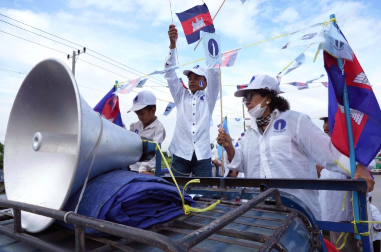 Candlelight party supporters hold Cambodian flags as they campaign on the back of a truck fitted with a loudhailer