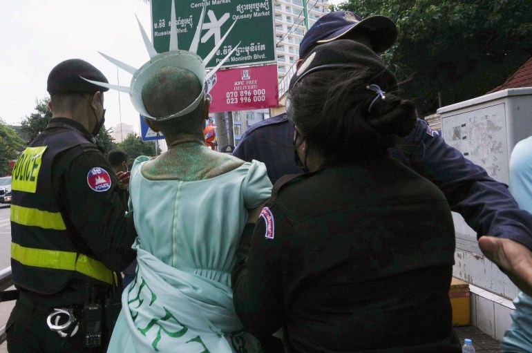 Theary Seng, dressed in a lime green dress as 'Lady Liberty' is marched away by Cambodian police.