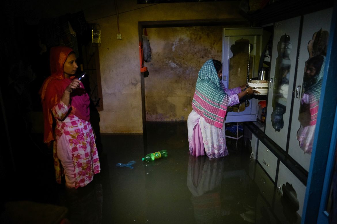 Two women stand inside a flooded home in Sylhet