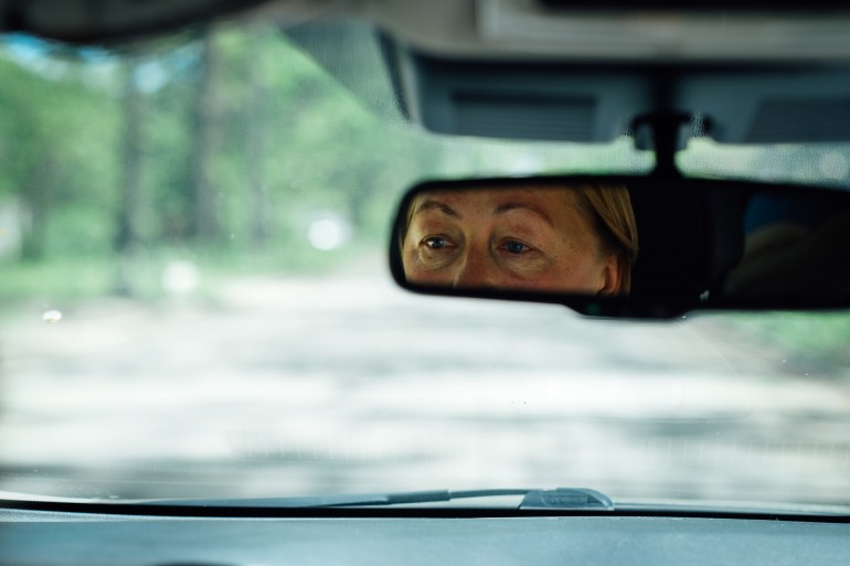 A photo of the front window of a car as viewed from inside the car with a woman reflected in the mirror,