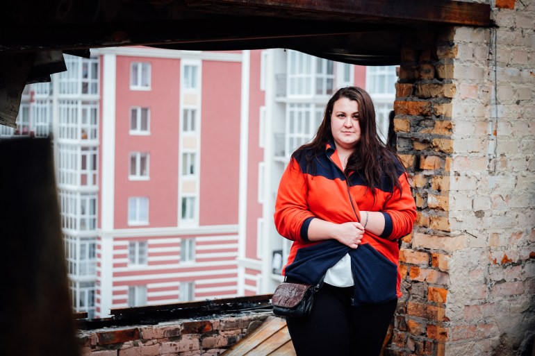 A photo of Anna Hlyvenko standing in front of a large hole on the side of an apartment building that once had a window.
