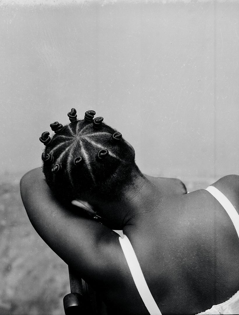 A photo of a woman from the back, with her head down in one of her arms.