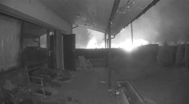 A photo of a CCTV still of an explosion viewed from the backyard of a house.