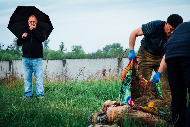 A photo of Oleksandr Bugeruk looking on as his mother's body is placed on the ground.