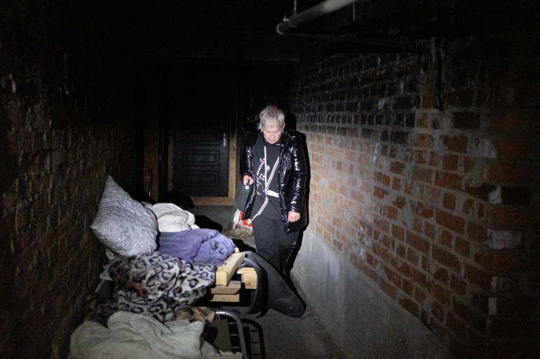 A photo of a woman standing next to a bed in a dark hall.