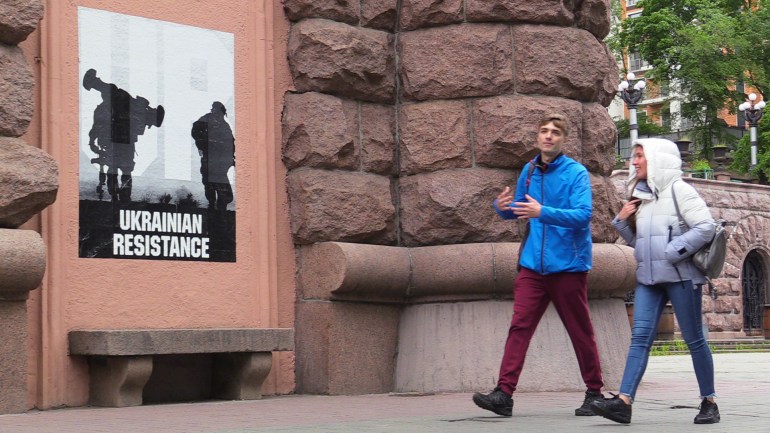 Young Ukrainians in central Kyiv next to a war-time poster