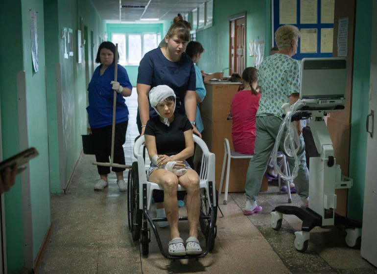 A hospital nurse pushes a wheelchair carrying a woman wounded by the Russian rocket attack at a shopping centre in a city hospital in Kremenchuk