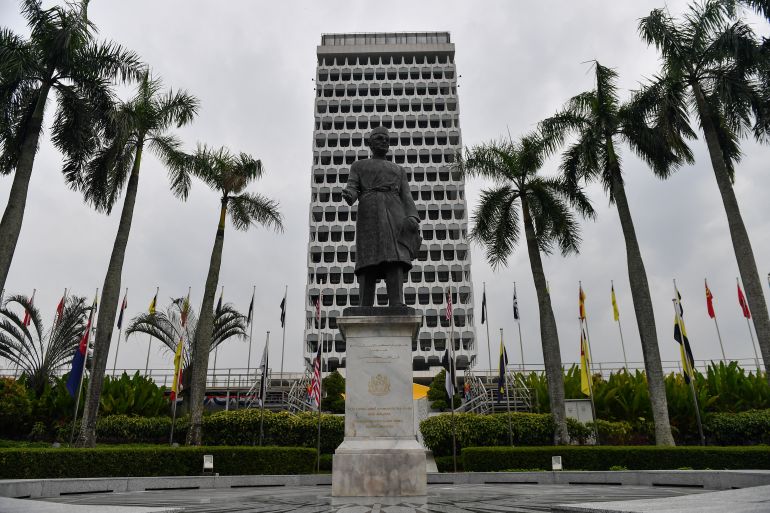 Exterior of Malaysia's parliament building with palm trees and a statue of the country's first prime minister tunku abdul rahman