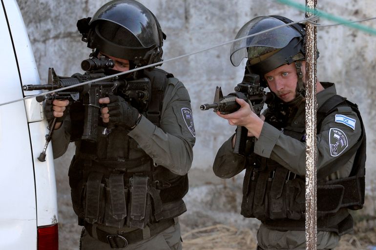 Israeli border guards wearing helmets and bullet-proof vests take aim with guns