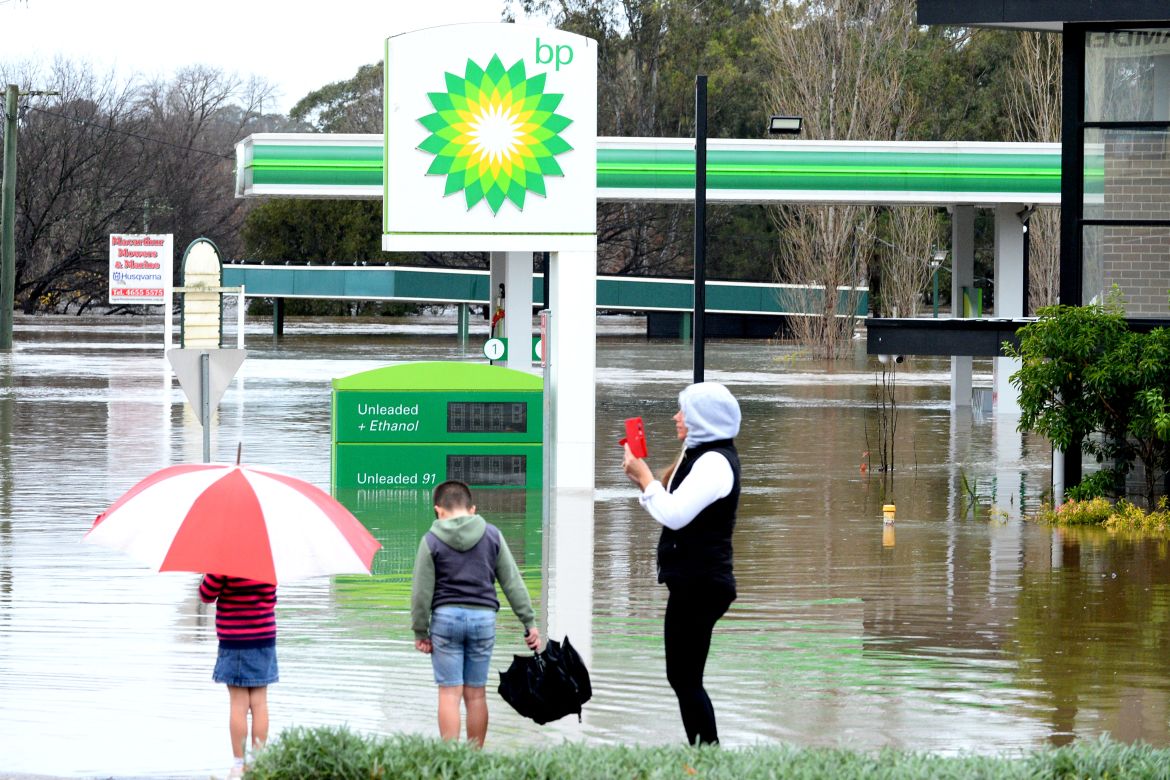 People stand next to a flooded petrol station