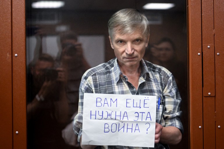 Moscow city deputy Alexei Gorinov, accused of spreading "knowingly false information" about the Russian army fighting in Ukraine, stands with a poster reading ""Do you still need this war?" inside a glass cell during the vedict hearing in his trial at a courthouse in Moscow