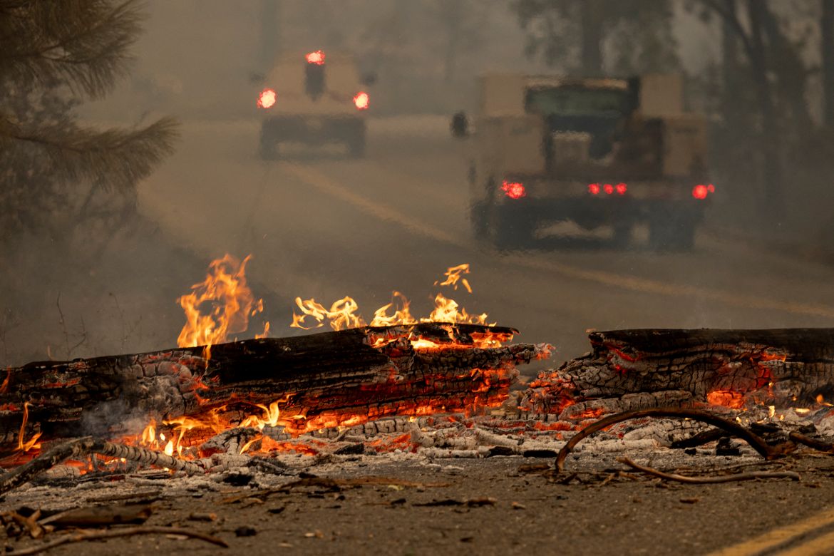 Vehicles pass a burning tree that fell across a road at the Oak Fire near Midpines