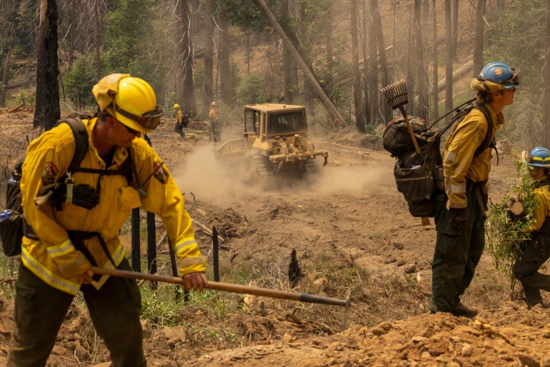 A bulldozer passes firefighters cutting vegetation to broaden a fireline at the Oak Fire near Mariposa, California, on July 25, 2022 Firefighters were battling California's largest wildfire of the summer on Monday, a blaze near famed Yosemite National Park that has forced thousands of people to evacuate, officials said. The Oak Fire in central California comes as parts of the United States remain in the grip of a sweltering heat wave.