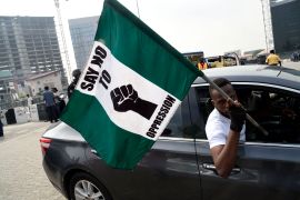 A man in a car carries the Nigerian national flag adorned with writing 'Say No To Oppression' during a protest