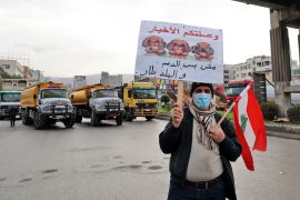 A Lebanese protester holds a sign as fuel tankers block a road in Lebanon's capital Beirut during a general strike by public transport and workers unions