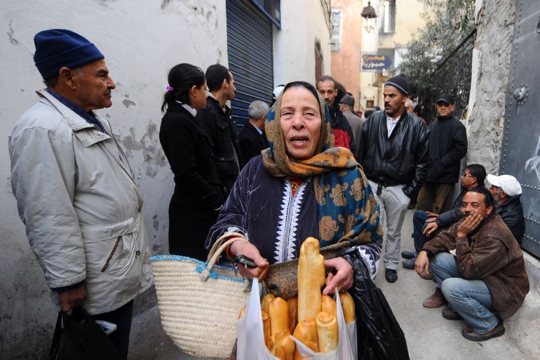 A woman shows bread she just bought while others queue up to buy some bread in Tunis's Medina on January 16, 2011.