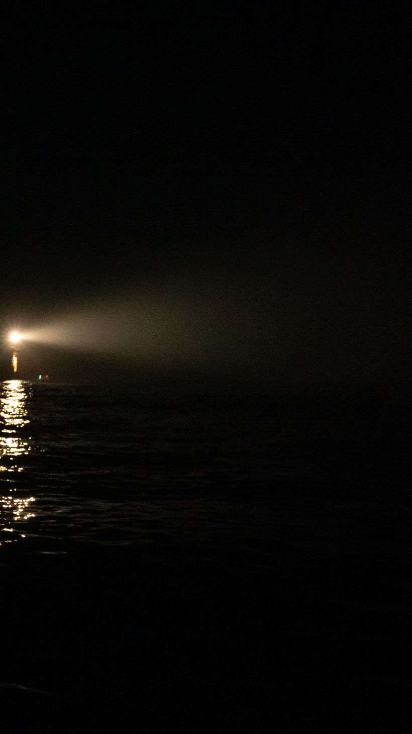 A ship's spotlight reflects on a small boat in distress