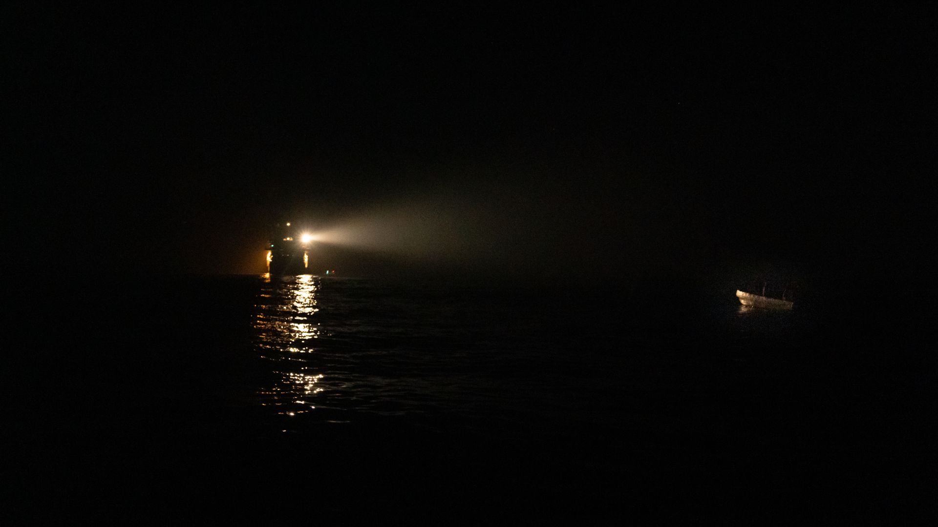 A ship's spotlight reflects on a small boat in distress