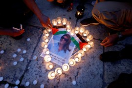 People light candles that form a heart around a photo of Shireen Abu Akleh during a vigil.
