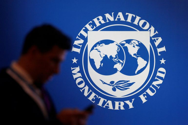 IMF logo on a wall with the silhouette of a man looking at his phone in the foreground.