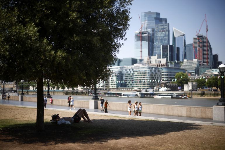 A person is seen resting in the shade on a bank of the river Thames